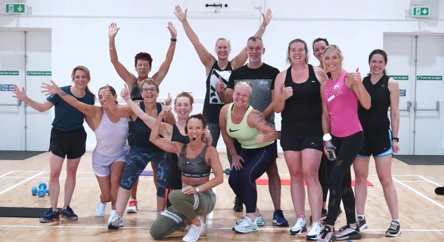 A high-energy group fitness class posing for a photo in the Main Hall after a workout session.