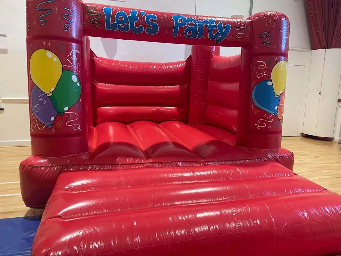A large, bright red inflatable bouncy castle set up on the hardwood floor of the Main Hall for a children’s party.