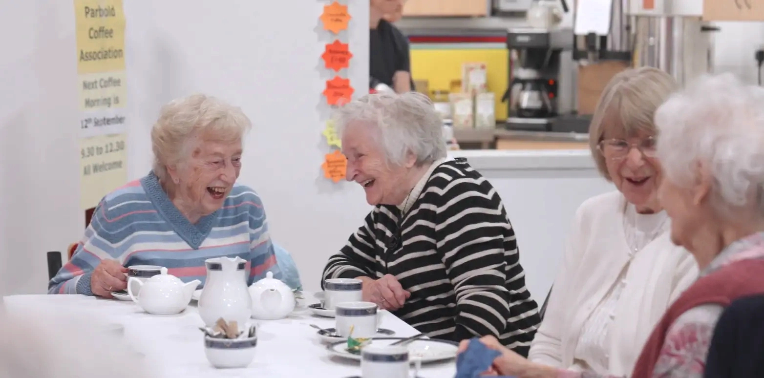 Senior community members enjoying tea and conversation during a social event in the village hall’s meeting space.